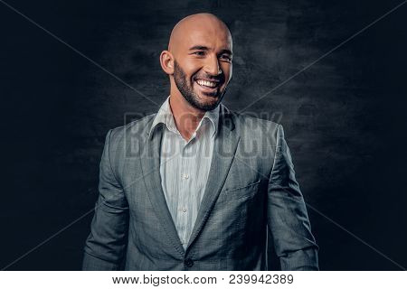 Positive Shaved Head Male Dressed In A Grey Suit Over Dark Grey Background.