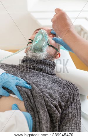 Male Patient With Oxygen Mask On His Face Is Lying On A Hospital Bed, In The Emergency Room