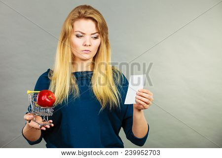 Worried Woman Holding Shopping Basket With Fruits Looking At Bill Receipt Being Scared Of Huge Price