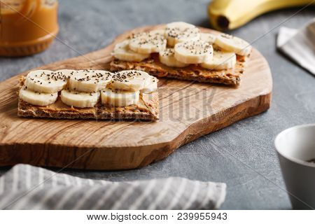 Two Toasts From Multi Grain Breads With Peanut Paste, Banana Slices And Chia Seeds On A Serving Wood