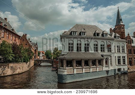 Bruges, Belgium - July 05, 2017. Old Brick Buildings, Bridge And Tower On The Canal Edge In A Sunny 