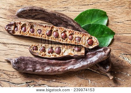 Carob pods and carob beans on the wooden table.