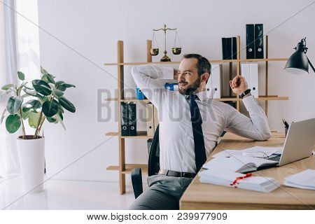 Lawyer Stretching While Sitting At Workplace With Laptop In Office