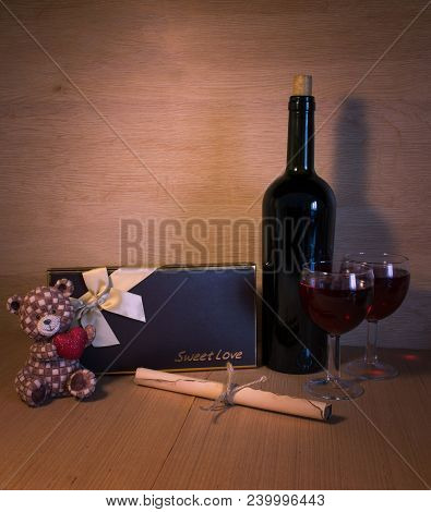 On The Table Is A Bottle Of Red Wine, Two Glasses, A Letter And A Gift