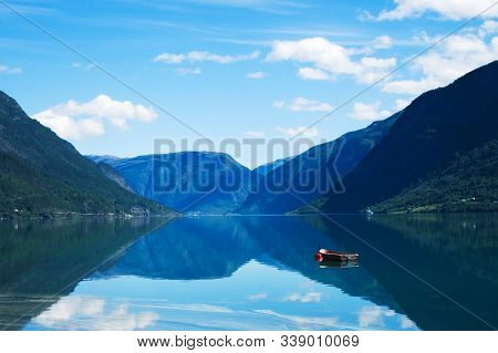 Small Wooden Boat Moored To A Red Buoy Floats On Waters Of The Lustrafjord In Norway, With Reflectio