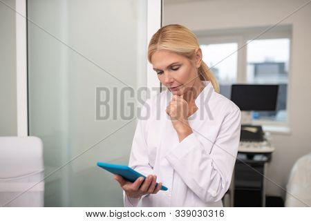 Blond Pleasant Doctor Holding Tablet In Her Hand