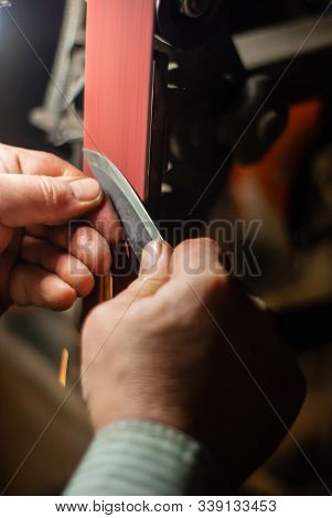 The Hands Of A Locksmith Sharpening The Workpiece For A Knife On A Grinding Belt