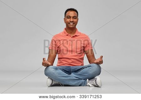 meditation, mindfulness and people concept - happy indian mant meditating in lotus yoga pose over gray background