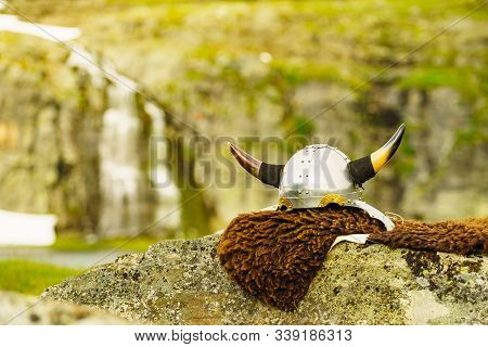 Equipment Of Viking Or Barbarian Warrior Outdoor On Nature. Viking Helmet On Brown Fur Of Animal In 