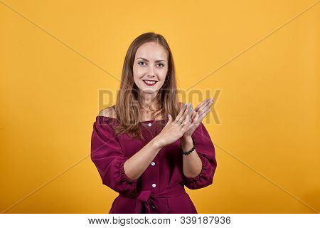 Young Girl Applouding And Smiling Over Isolated Orange Wall. She Is Dressed Up In Burgundy Bluse. He