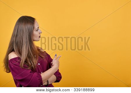 Girl In Burgundy Bluse Over Isolated Orange Background Undecided Pointing Finger With Doubts Looking