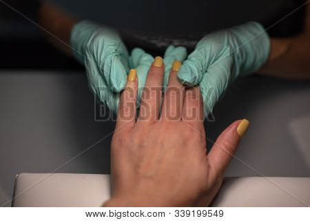 A Manicure Hand With A Nail Lies On A Manicure Hand In Blue Hygienic Gloves.hands On The Manicure Of