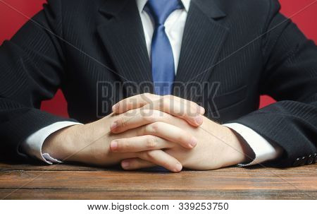 A Man Sits At The Table With Folded Arms. Ready To Listen To News And Criticism. Serious Talk. Calml
