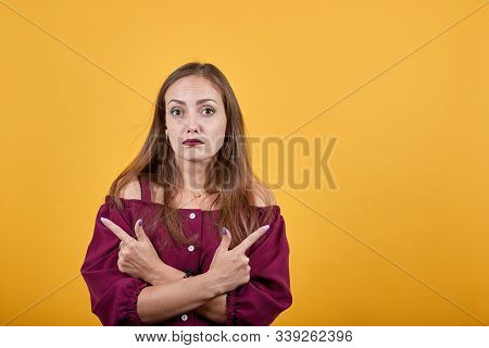 Girl In Burgundy Bluse Over Isolated Orange Background Undecided Pointing Fingers In Different Direc