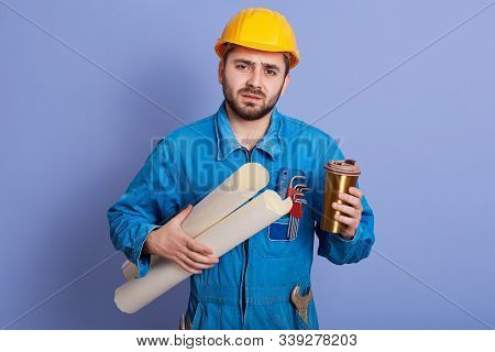 Tired Engineer Or Foreman In Protective Yellow Helmet And Blue Workwear Holding Blueprint In Hands A