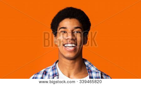 Human Emotions. Portrait Of Smiling Afro Teen Guy Loking At Camera On Orange Background