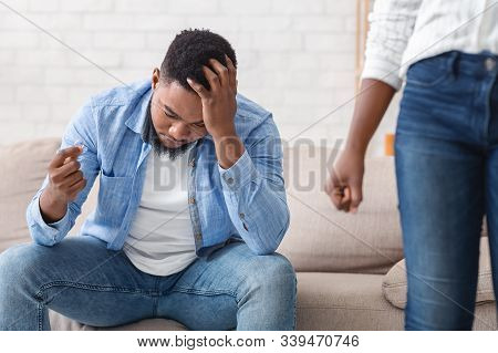 Breakup And Divorce Concept. Depressed Black Man Holding Gold Wedding Ring In Hand While His Wife Le