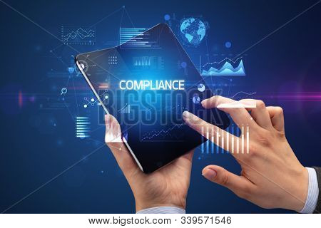 Businessman holding a foldable smartphone with COMPLIANCE inscription, successful business concept