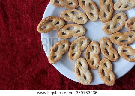 Flat Lay View Of A White Plate Filled With Krakeling A Very Popular Sort Of Dutch Cookie. Red Table 