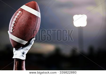 Hand of a player holding American football against close-up of soccer field