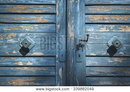 Rustic Wooden Door With Shriveled Blue Paint Close-up On Doorknobs. Antique Blue Wood Gate. Aged Woo