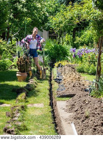 Young Woman Resting Leaning On Spade After Gardening. Gardener Digging Trench For Subsurface Irrigat