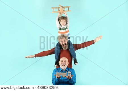 Three Different Generations Ages Grandfather Father And Child Son Playing With Toy Plane In Studio. 