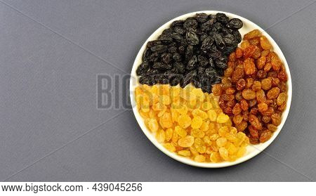 Raisins Are Light, Brown, Dark On A Round White Plate On A Gray Background. Top View. Space For Copy