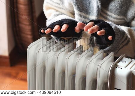 Person Heating Their Hands At Home Over A Domestic Portable Radiator In Winter