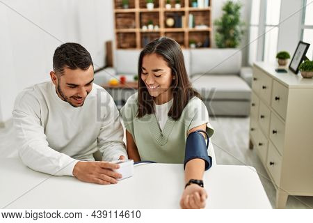 Young latin couple smiling happy measuring blood pressure using tensiometer at home.