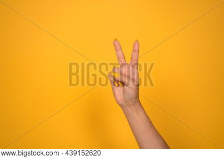 V Sign. Female Hand Shows Two Fingers Or Peace Gesture. Cut Out On Yellow Background. Copy Space.
