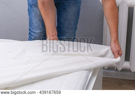 A Man Puts An Elasticated Sheet On The Mattress. Change Of Bed Linen.