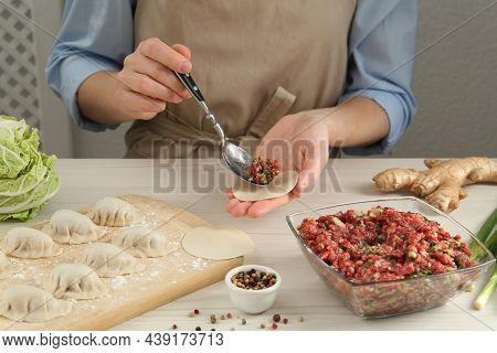 Woman Putting Gyoza Filling In Center Of Dough Wrapper At White Wooden Table, Closeup