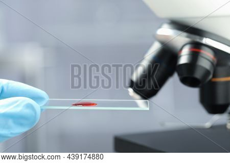 Scientist Holding Microscope Slide With Sample Of Red Liquid In Laboratory, Closeup