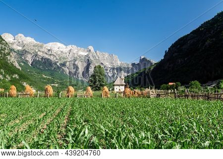A Path With Wooden Fence Leads The Catholic Church In The Theth Valley, On Background The Mountains 