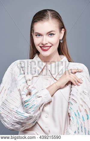 Haute couture fashion. Gorgeous young woman fashion model poses in extravagant beige blouse with wide sleeves. Studio portrait on a grey background.