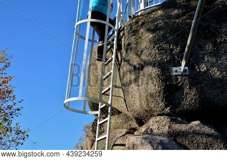 Galvanized Iron Gray Fire Ladder Leading To The Rock. Safety Is Ensured By A Tube-shaped Grille Of T
