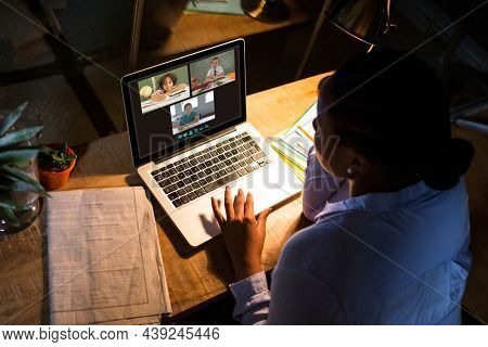 African american woman using laptop for video call, with diverse elementary school pupils on screen. communication technology and online education, digital composite image.