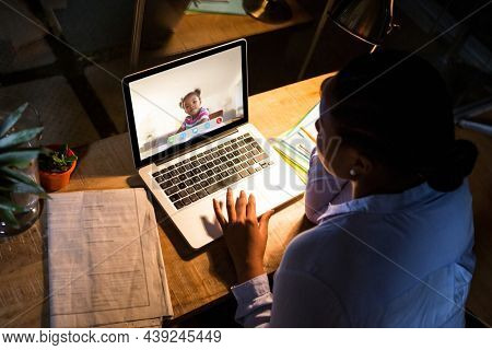 African american woman using laptop for video call, with elementary school pupil on screen. communication technology and online education, digital composite image.