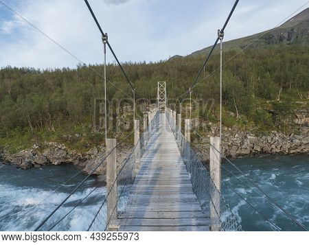 Wooden Pedestrian Suspension Bridge Over Vuojatadno River Rapids On Background Of Lapland Sweden Art