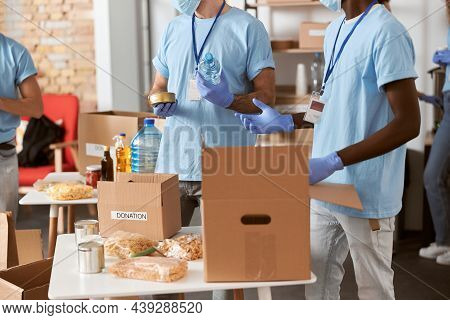 Cropped Shot Of Mutiethnic Volunteers In Blue Uniform, Protective Gloves Separating Donations Stuffs
