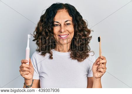 Middle age hispanic woman holding electric toothbrush and teethbrush smiling with a happy and cool smile on face. showing teeth. 