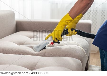 Close-up Of Housekeeper Holding Modern Washing Vacuum Cleaner And Cleaning Dirty Sofa With Stain Wit