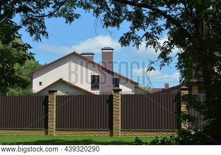 A Modern Stucco House With An Exterior Chimney Behind A Metal Fence With Brick Foundation And Fence 