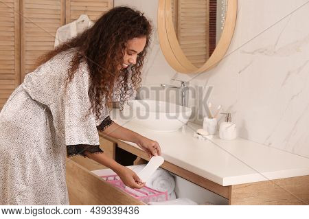 Young African American Woman Taking Pantyliner Out Of Drawer In Bathroom