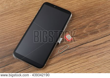 Sim Card, Mobile Phone And Ejector Tool On Wooden Table