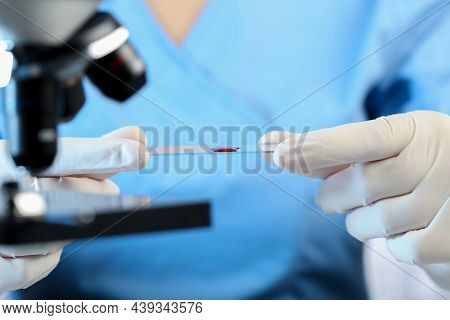 Scientist Holding Microscope Slide With Sample Of Red Liquid In Laboratory, Closeup