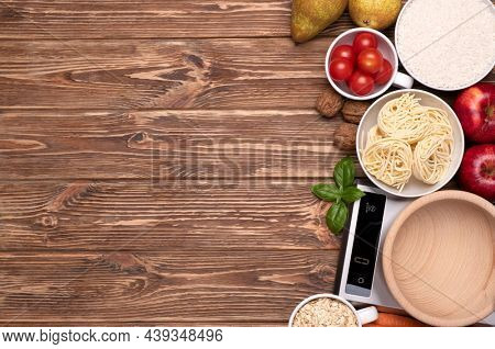 Kitchen scales and various food samples on wooden background, top view with copy space