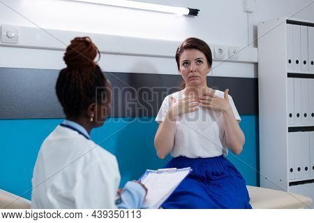 Woman Patient Standing On Medical Bed Explaining Disease Symptoms To African American Therapist Doct