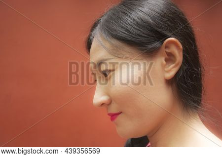 A Happy Chinese Woman Looking Away Against A Rust Colored Wall Within Chengdu China.
